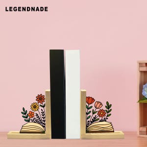 May include: Wooden bookends with floral designs and the text "LEGENDNADE" at the top. The bookends feature a black and a white book between them. The floral designs include orange, yellow, and red flowers with green leaves.
