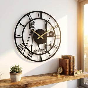 Könnte beinhalten: Eine große, runde Wanduhr aus schwarzem Metall mit römischen Ziffern und einem zentralen Motiv aus einem Vermessungsgerät auf einem Stativ, einer Nivellierlatte, einer Windrose und einer aufgerollten Karte. Zwei goldene Zeiger liegen mittig.