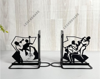 Puede incluir: Juego de sujetalibros de metal negro con siluetas de músicos de jazz. Cada sujetalibros representa un conjunto musical diferente, con instrumentos como trompeta, saxofón y contrabajo. Los sujetalibros tienen una base rectangular y un soporte vertical.