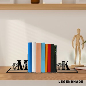 May include: Black metal bookends with floral accents and the letters "M" and "K" holding a row of colorful books. The bookends have the names "Michael" and "Katherine" on them. The word "LEGENDNADE" is at the bottom.