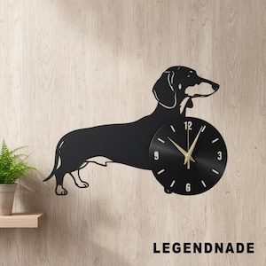 May include: Black metal dachshund dog wall clock with gold hands and numbers. The clock is attached to the dog's body. The text "LEGENDNADE" is at the bottom.