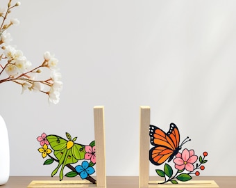May include: Wooden bookends featuring a green moth and an orange butterfly with floral accents. The bookends are made of light-colored wood and are designed to hold books upright. The word "LEGENDNADE" is printed at the top.
