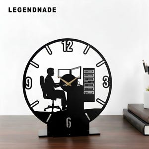 May include: Black desk clock with a silhouette design. The clock features a person sitting at a computer with two monitors, a server rack, and the numbers 3, 6, 9, and 12. The clock hands are gold. The word LEGENDNADE is at the top.