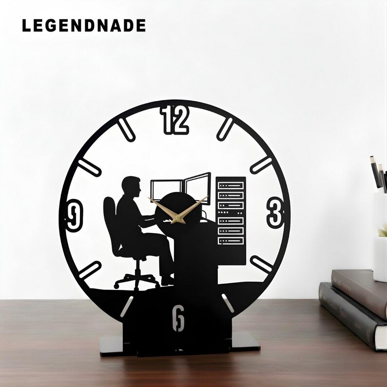 May include: Black desk clock with a silhouette design. The clock features a person sitting at a computer with two monitors, a server rack, and the numbers 3, 6, 9, and 12. The clock hands are gold. The word LEGENDNADE is at the top.