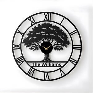 Könnte beinhalten: Schwarze Metall-Wanduhr mit Baumdesign und römischen Ziffern. Das Zifferblatt enthält den Text "The Williams" und goldfarbene Zeiger. Die Uhr ist rund und hat einen modernen, minimalistischen Stil.