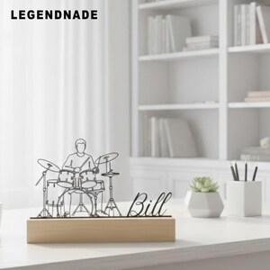 May include: A black wireframe sculpture of a drummer playing a drum set, mounted on a light wood base. The name "Bill" is written in cursive script. The word "LEGENDNADE" is printed in bold, black capital letters at the top.
