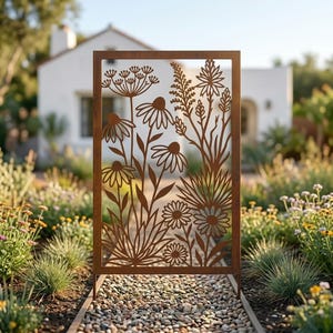 May include: A rectangular metal garden screen featuring a laser-cut design of various wildflowers and grasses. The panel has a rusted brown finish and is supported by two thin metal legs, creating a decorative barrier for outdoor spaces.