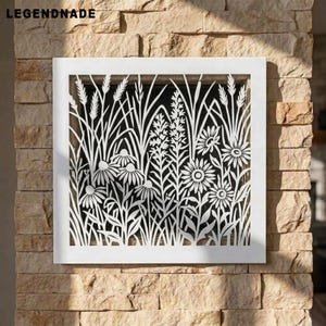May include: A square white metal wall panel featuring a laser-cut design of wildflowers and tall grasses. The intricate cutout pattern displays various floral shapes and slender stalks, creating a detailed botanical silhouette against a dark background.