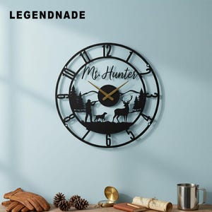 May include: Black metal wall clock with a hunting scene silhouette. The clock features Roman numerals, gold hands, and the text "Mr. Hunter". The scene includes a hunter, dog, deer, and trees. The brand name "LEGENDNADE" is at the top left.