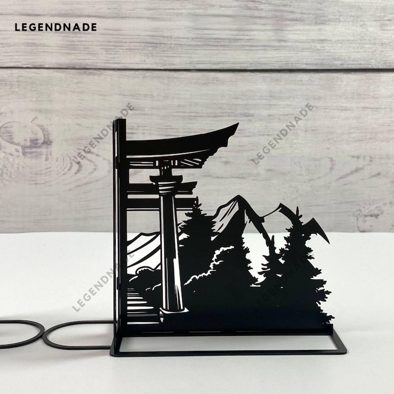 May include: Black metal bookends featuring a silhouette of a Japanese temple gate, mountains, and trees. The bookends are designed to hold books upright.