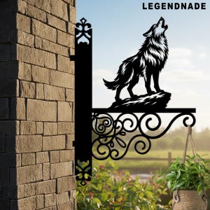 May include: Black metal sign featuring a howling wolf silhouette atop a rock, with decorative scrollwork and the text "LEGENDNADE". The sign is mounted on a brick wall, with a hanging basket of plants visible.