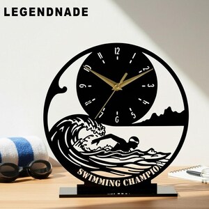 Könnte beinhalten: Schwarze und goldene Schreibtischuhr mit Schwimmthema. Die Uhr zeigt einen Schwimmer im Wasser, Wellen und die Worte "SWIMMING CHAMPION". Die Uhr hat goldene Zeiger und ein schwarzes Zifferblatt. Der Markenname "LEGENDNADE" steht oben.