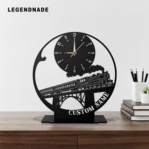 Puede incluir: Reloj de metal negro con diseño de tren. La esfera del reloj está integrada en el diseño, con una imagen de tren debajo. El texto "CUSTOM NAME" está en la parte inferior. La marca "LEGENDNADE" está en la parte superior.