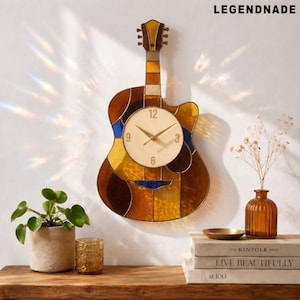 May include: A guitar-shaped wall clock with a stained-glass design in shades of brown, yellow, and blue. The clock face is cream-colored with gold hands and black numerals. The brand name "LEGENDNADE" is displayed at the top.