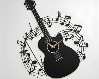Könnte beinhalten: Eine schwarze Wanduhr in Form einer akustischen Gitarre, umgeben von einem kreisförmigen Metalldesign aus Notenlinien und Noten. Die Uhr hat goldfarbene Zeiger in der Mitte des Gitarrenkörpers. Der Text LEGENDNADE ist unten links in Schwarz aufgedruckt.