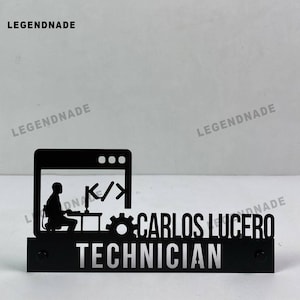 Może przedstawiać: Czarny metalowy znak na biurko z sylwetką osoby przy komputerze, symbolami kodu i napisem "CARLOS LUCERO TECHNICIAN" w srebrnych literach. Znak ma prostokątną podstawę z dwiema małymi czarnymi śrubami.