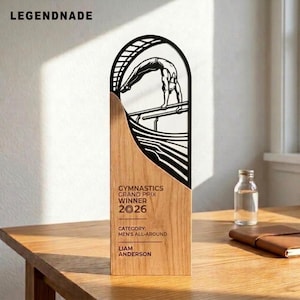 May include: A wooden trophy featuring a black arched cutout with a silhouette of a gymnast on parallel bars. The wood surface is engraved with the text: GYMNASTICS GRAND PRIX WINNER 2026, CATEGORY: MEN'S ALL-AROUND, and the name LIAM ANDERSON.