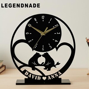 Könnte beinhalten: Schwarze Laser-Holzuhr mit rundem Zifferblatt und goldenen Zeigern. Die Uhr zeigt zwei küssende Bärensilhouetten mit den Namen "DAVID" und "ANNA" darunter. Der Markenname "LEGENDNADE" steht oben.
