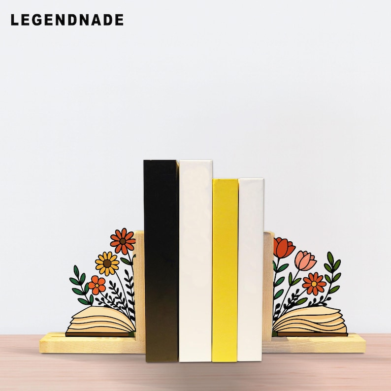 May include: Wooden bookends with a floral design. The bookends feature a black, white, and yellow color scheme. The text "LEGENDNADE" is in the upper left corner. The bookends are designed to hold books.