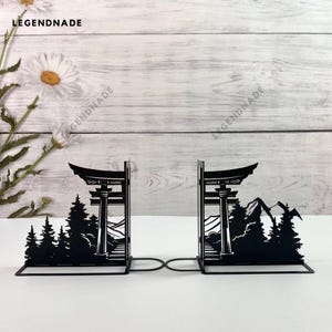 Könnte beinhalten: Schwarze Metall-Buchstützen in Form eines japanischen Tempeltores mit einem Berg und Bäumen im Hintergrund.