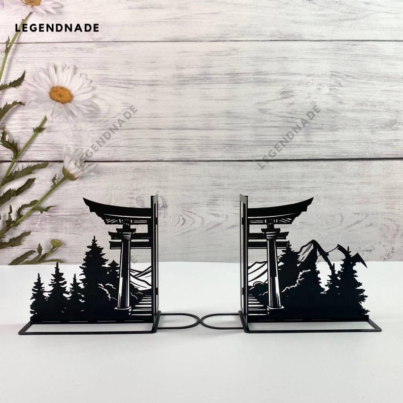 May include: Black metal bookends shaped like a Japanese temple gate with a mountain and trees in the background.