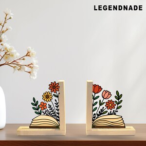 May include: Two wooden bookends with floral designs. Each bookend features a light-colored wooden base and upright support. The floral designs include orange, yellow, and pink flowers with green leaves. The text "LEGENDNADE" is at the top.