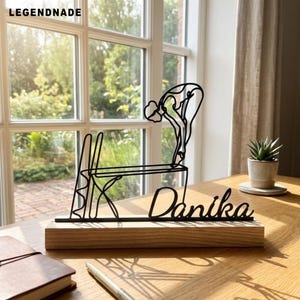 May include: A black wire sculpture depicting a swimmer on a diving board, mounted on a rectangular wooden base. The sculpture features the name Danika in cursive script. The text LEGENDNADE is visible in the upper left corner of the image.