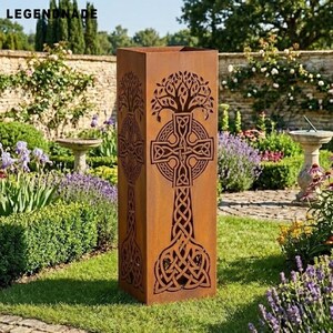 May include: A weathered metal garden planter with a Celtic cross and tree of life design. The brown, rectangular planter is set in a garden with flowers and shrubs. The word "LEGENDNADE" is visible at the top. The planter is approximately 100 cm tall.