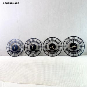 May include: Four black metal wall clocks with Roman numeral hour markers and gold-colored hands. Each clock displays a different city name: Moscow, London, Tokyo, and New York. The clocks are arranged in a row, varying in size.