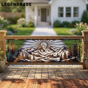 May include: A rectangular metal railing insert featuring a laser-cut landscape design with a sunburst, mountain peaks, pine trees, and a small cabin. The metal has a multi-toned finish with bronze, blue, and brown hues. Text reads LEGENDNADE.