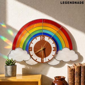 May include: A stained glass wall clock shaped like a rainbow with white clouds at the base. The clock face is circular with a brown center, white border, and brown numerals 3, 6, 9, and 12. The text LEGENDNADE appears in the top right corner.