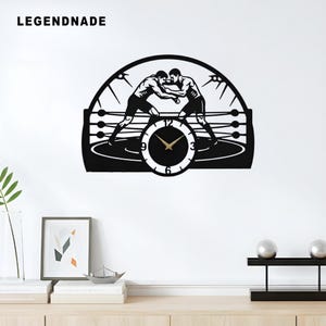 Könnte beinhalten: Schwarze Wanduhr mit einem Boxring-Design und zwei Figuren in der Mitte. Die Uhr hat ein rundes Zifferblatt mit goldenen Zeigern und den Zahlen 3, 6, 9 und 12. Das Wort "LEGENDNADE" steht oben links.
