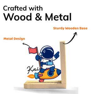 May include: A wooden and metal desk organizer featuring a cartoon astronaut on a rocket. The design includes a red flag and the name "Kai". The text "Crafted with Wood & Metal" and "Sturdy Wooden Base" are also visible.