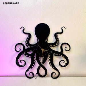 Op de afbeelding: Zwarte octopus wandklok met gouden wijzers. De klok heeft een uniek ontwerp met acht tentakels en de tekst "LEGENDNADE" linksboven. De klok is aan een witte muur bevestigd.