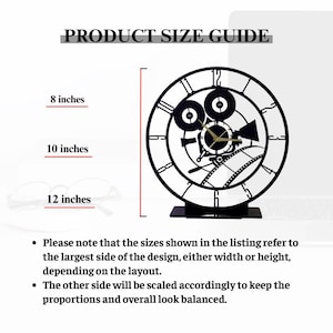 May include: Black metal clock with a film camera design. The clock face features Roman numerals and gold-colored clock hands. The image includes a product size guide with dimensions of 20, 25, and 30 cm. The text reads "PRODUCT SIZE GUIDE".