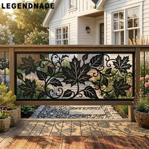 May include: A black metal railing panel featuring a decorative laser-cut design of maple leaves and swirling vines. The rectangular panel is framed by natural wood posts and rails, positioned on a wooden deck overlooking a garden path.