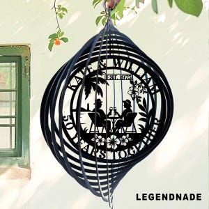 May include: Black metal wind spinner with a spiral design. The center features a silhouette of a couple at a table, palm trees, and the text "KATE & WILLIAM EST. 1975" and "50 YEARS TOGETHER". The word "LEGENDNADE" is at the bottom.