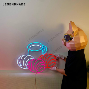 May include: Neon sign depicting a blue coffee cup and three pink pastries. The sign is lit up and hanging on a white wall.