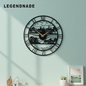 Puede incluir: Reloj de pared de metal negro con un diseño recortado de un pueblo. El reloj presenta números romanos, manecillas doradas y el texto "The Millers" en la parte inferior. La marca "LEGENDNADE" está en la parte superior.