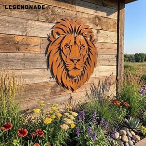 Op de afbeelding: Een roestkleurig metalen wanddecoratie in de vorm van een leeuwenkop met een gedetailleerde manen, voorzien van de tekst LEGENDNADE in de linkerbovenhoek. De leeuw heeft een symmetrisch gezicht met scherpe, hoekige uitsparingen in de manen.