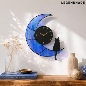 May include: A wall clock featuring a blue stained-glass crescent moon design with a black clock face and gold hands. A black cat silhouette sits on the moon. The word LEGENDNADE is at the top.