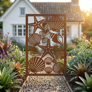 May include: A rectangular metal garden screen with a rust-colored finish featuring a laser-cut pattern of various seashells and two starfish. The panel is positioned vertically on a gravel path, displaying a detailed cutout design of marine life.