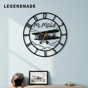 May include: Black metal wall clock with a biplane design, featuring the name "Mr. Mitchell". The clock has gold-colored hands and Roman numerals. The brand name "LEGENDNADE" is at the top left.