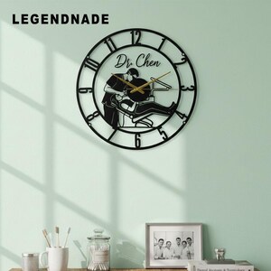 May include: Black metal wall clock featuring a dentist and patient silhouette. The clock has Roman numerals and the name "Dr. Chen". Gold clock hands. The brand name "LEGENDNADE" is at the top left.