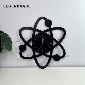 May include: Black atomic clock with red hands, featuring a unique atom design. The clock has a circular face with numbers and the brand name "LEGENDNADE" at the top. A modern wall decor piece.