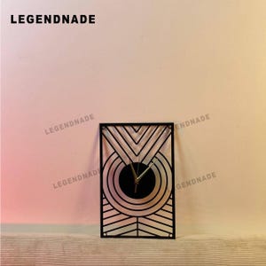 May include: Black geometric wall clock with a circular clock face and gold hands. The clock is rectangular with a decorative, openwork design. The word "LEGENDNADE" is printed at the top.