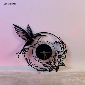 May include: Black metal wall clock with a hummingbird design and floral detailing. The clock face is black with Roman numerals. The name "DONOFRIO" is written on the clock. The brand name "LEGENDNADE" is at the top left.
