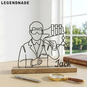 Può includere: Scultura in filo di metallo nero di uno scienziato con attrezzature da laboratorio, montata su una base di legno. Il nome "Jack" è scritto in corsivo. La parola "LEGENDNADE" è in alto.