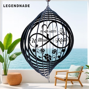 Peut inclure: Mobile éolienne en métal noir avec un design en spirale. Le centre présente un cœur, un papillon, des motifs floraux et les noms "William & Kate" avec la date "10-06-2015". Le mot "LEGENDNADE" est dans le coin supérieur gauche.