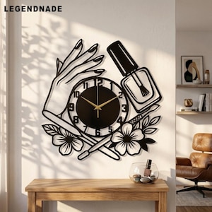 Könnte beinhalten: Eine schwarze Wanduhr mit einem ausgeschnittenen Design einer Hand mit manikürten Nägeln, einer Nagellackflasche und floralen Akzenten. Das runde Zifferblatt hat schwarze Zahlen und goldfarbene Zeiger. Der Text LEGENDNADE ist oben links zu sehen.